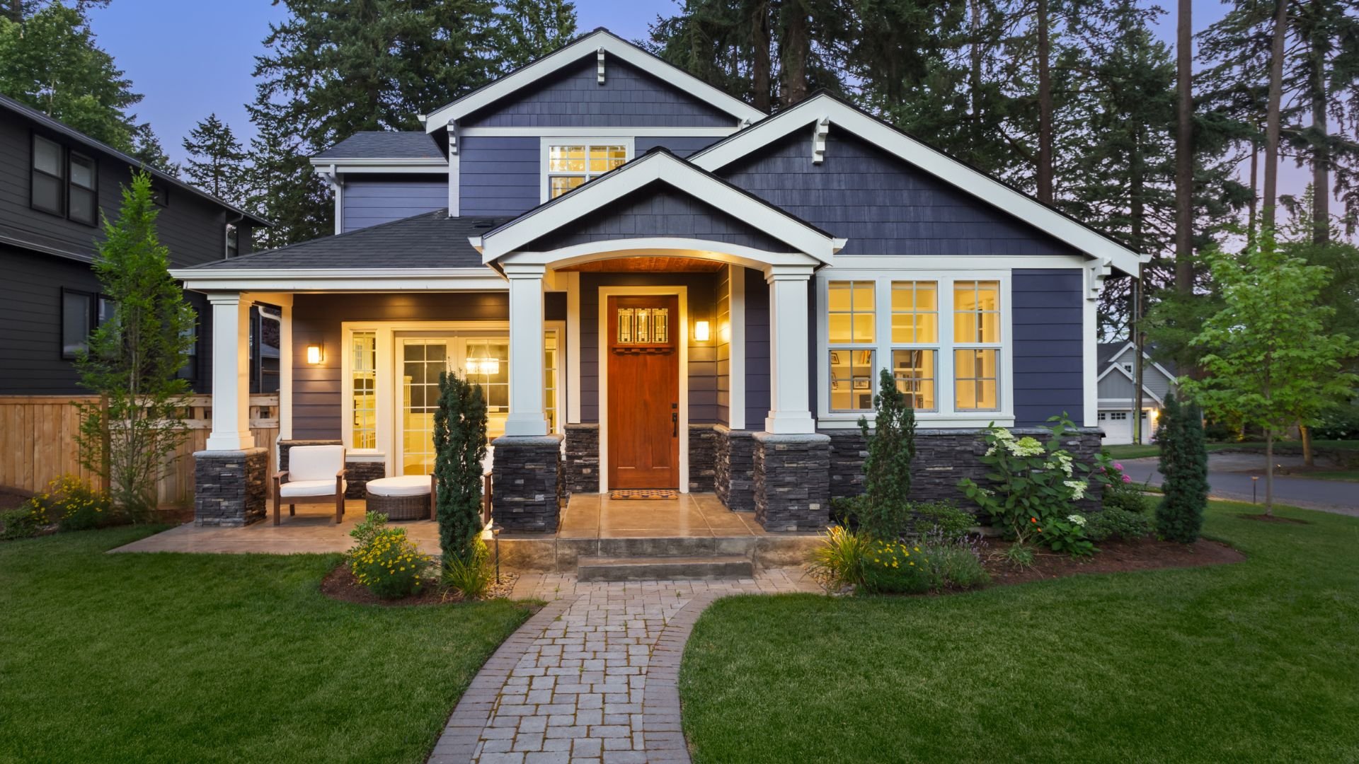 Craftsman-style house with blue siding, white trim, and stone accents at dusk