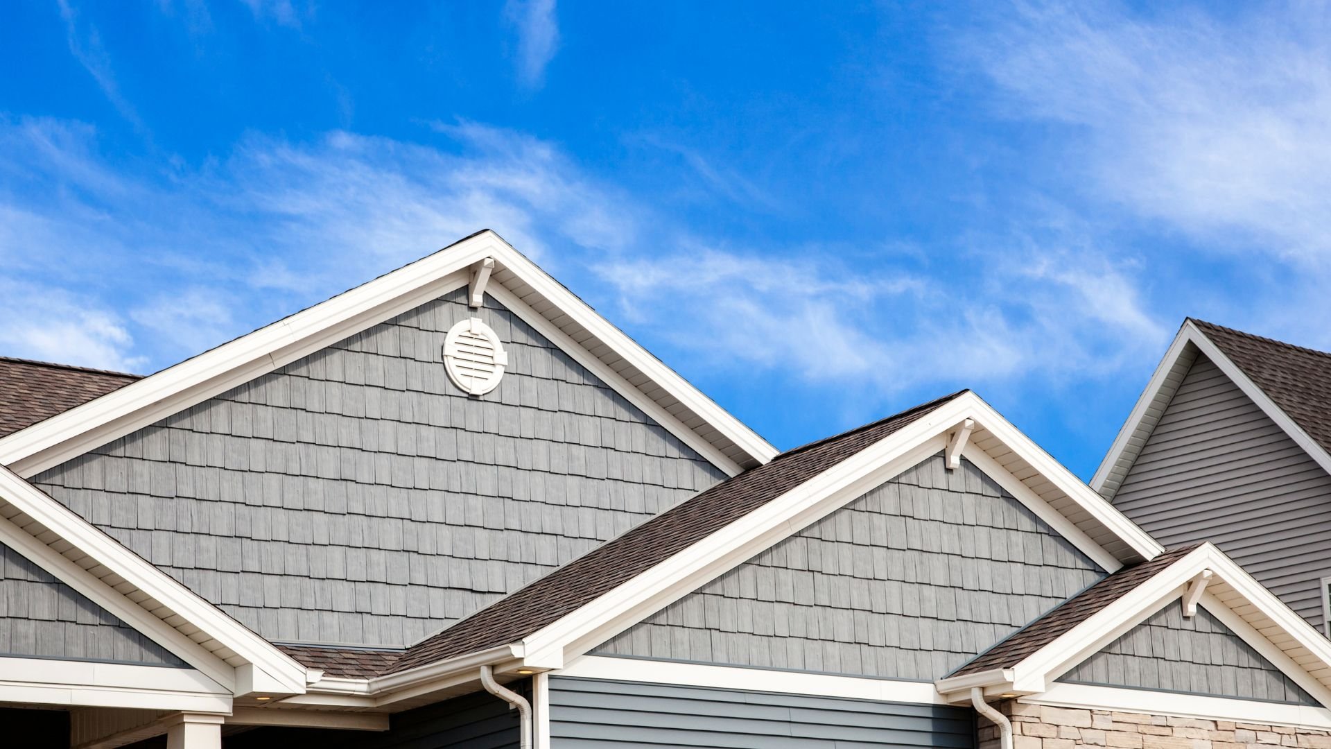 Modern suburban houses with gray siding and brown roofs against blue sky