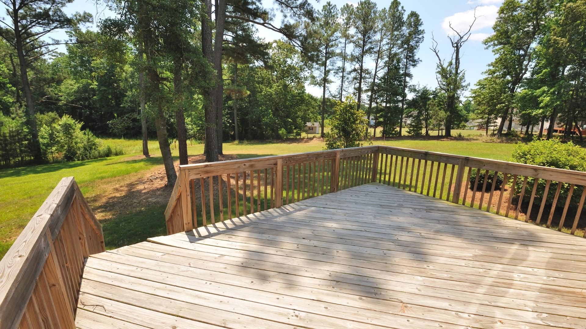 Wooden deck overlooking green yard and pine trees on sunny day