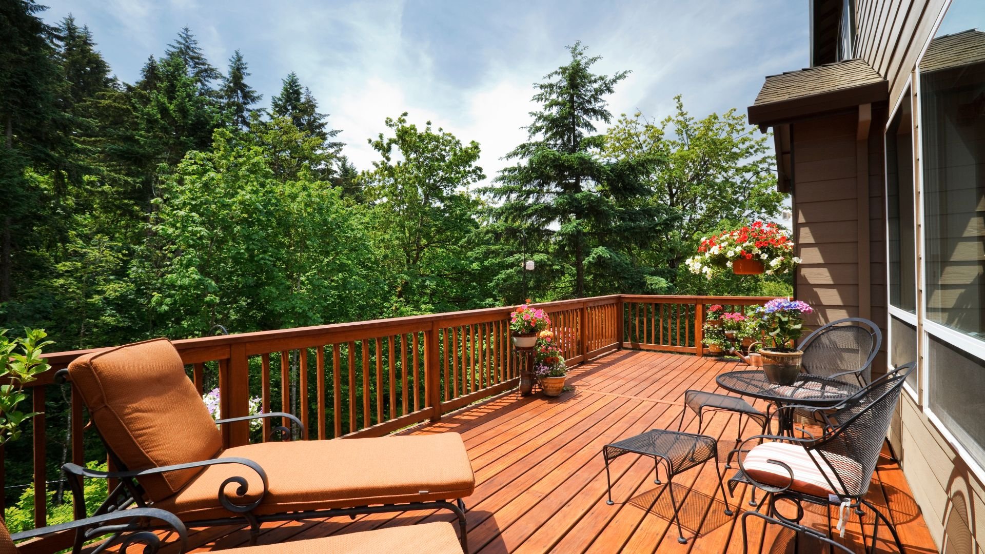 Wooden deck with lounge chair and potted flowers overlooking lush forest