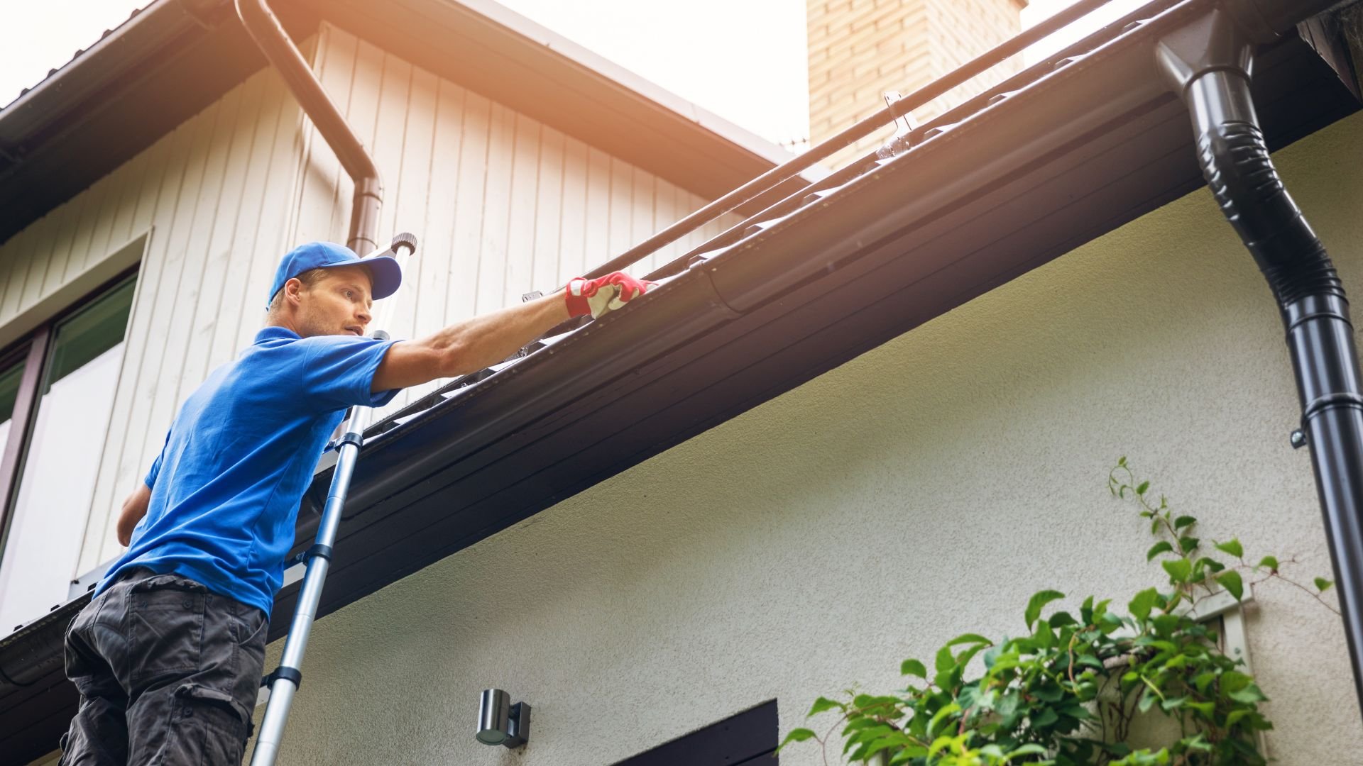 Worker on ladder cleaning gutters of a residential house
