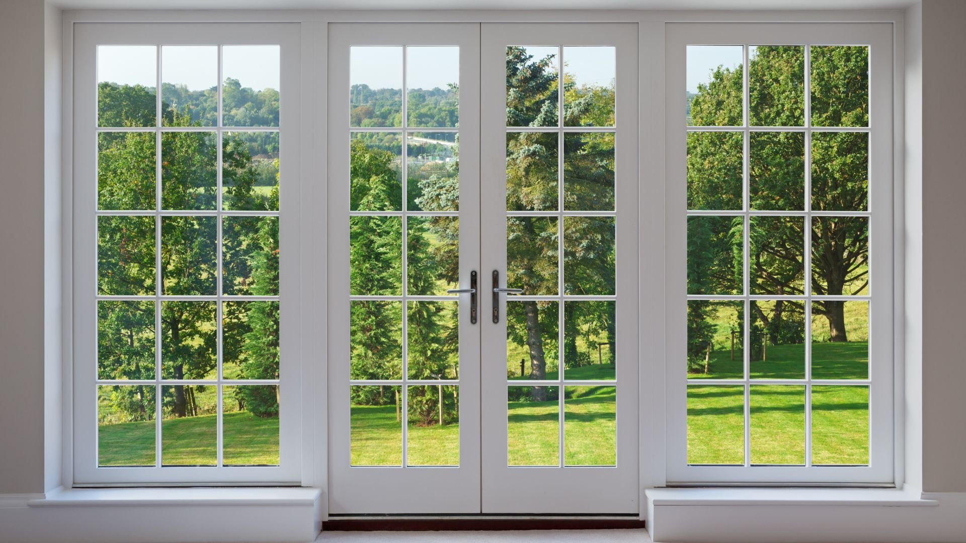 White French doors open to lush green garden with trees and lawn